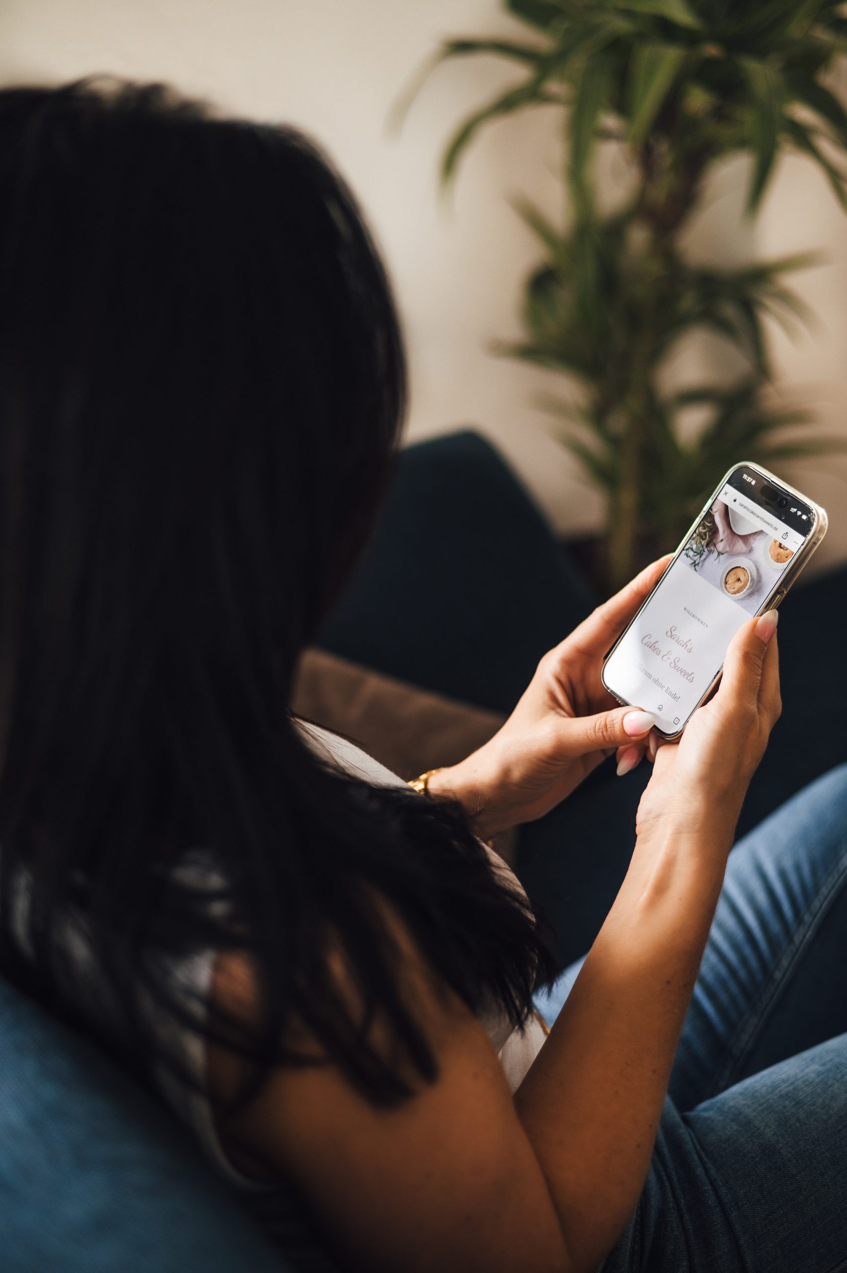 Sarah Sangermann sitzt entspannt auf dem Sofa und betrachtet ihre eigene Website auf dem Smartphone