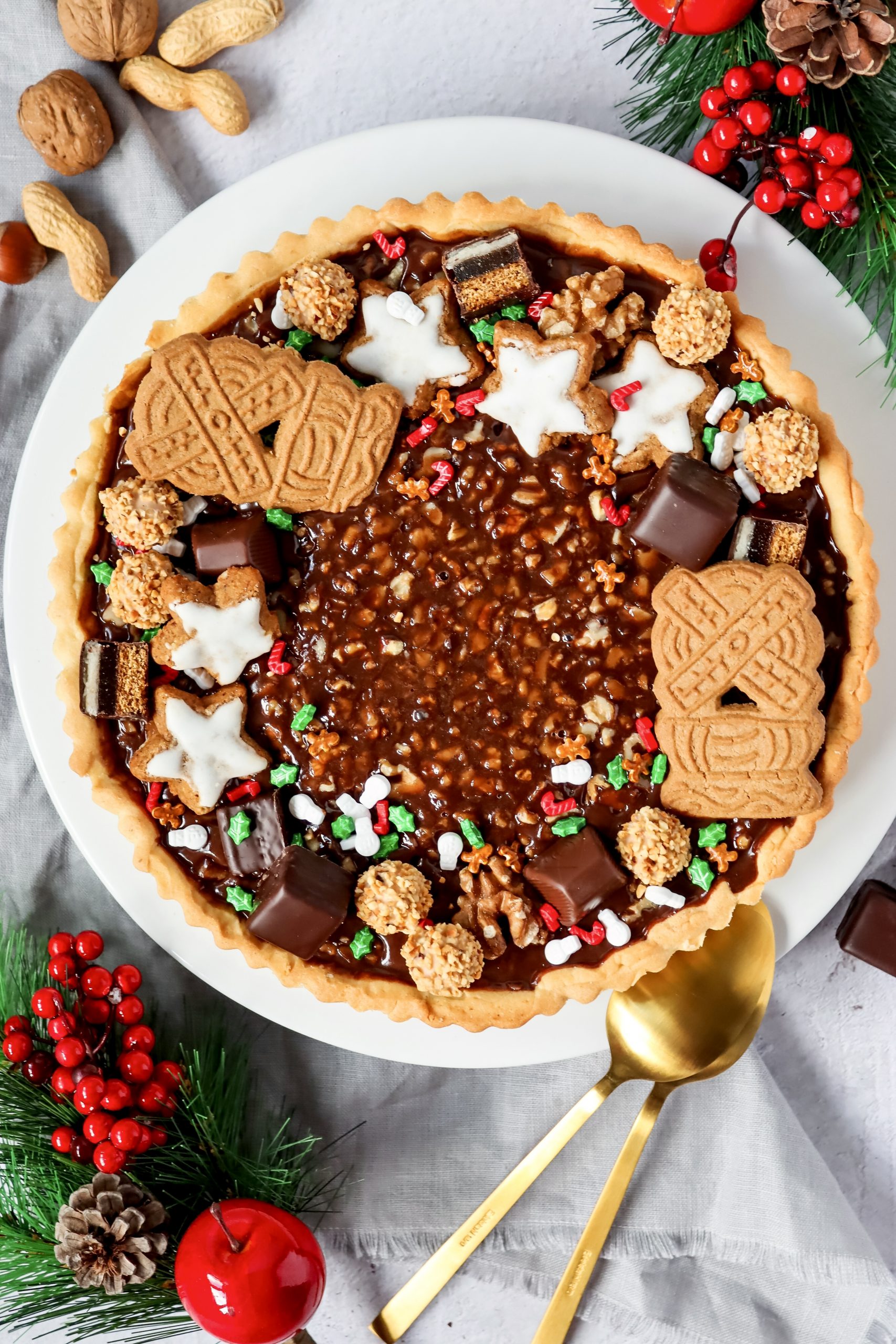 Schokoladen-Walnusstarte Schokoladen-Walnuss-Tarte mit Mürbeteigboden, Schokokaramellfüllung und winterlicher Dekoration aus Keksen, Pralinen und Nüssen.