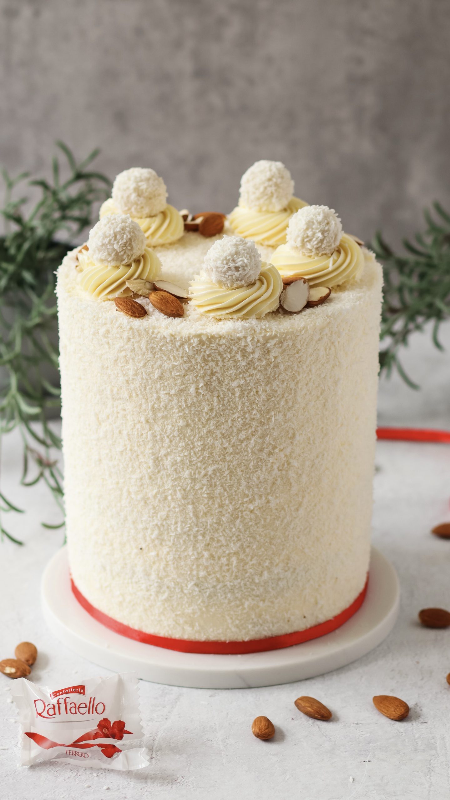 Home Hohe Raffaello Torte mit Kokosraspeln und Raffaello Pralinen auf einer Tortenplatte