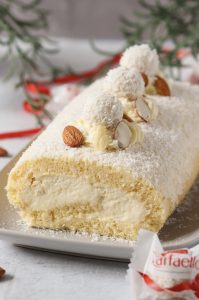 Raffaello-Biskuitrolle Raffaello-Biskuitrolle mit luftiger Kokoscreme und Raffaello-Füllung auf einer weißen Servierplatte
