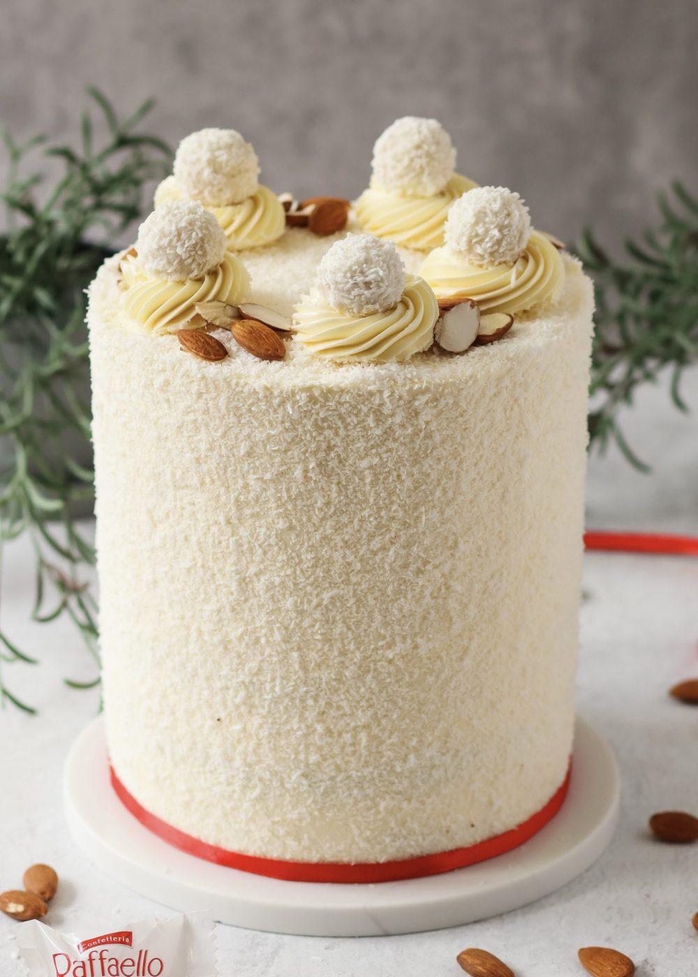 Hohe Raffaello Torte mit Kokosraspeln und Raffaello Pralinen auf einer Tortenplatte