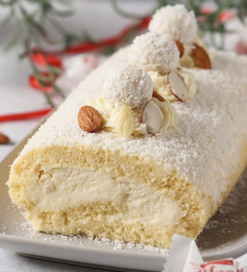 Raffaello-Biskuitrolle mit luftiger Kokoscreme und Raffaello-F&uuml;llung auf einer wei&szlig;en Servierplatte