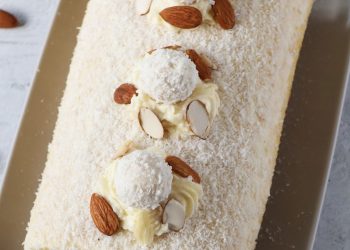 Draufsicht einer Raffaello-Biskuitrolle mit Kokosraspeln, Raffaellos und Mandelbl&auml;ttchen