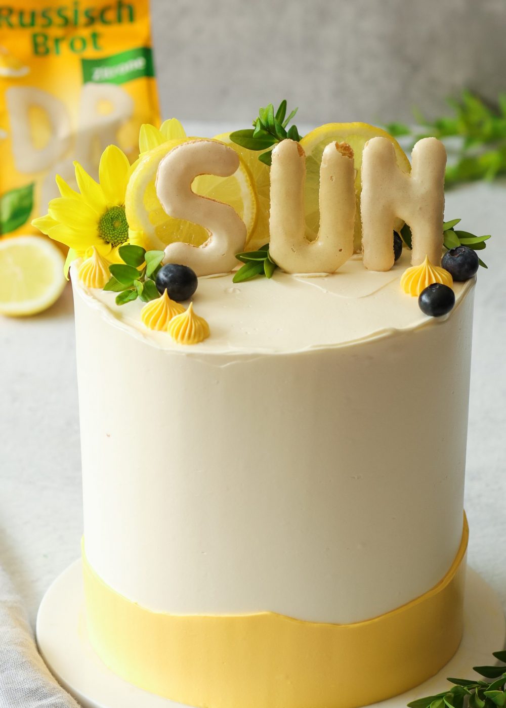Zitronentorte mit Lemon Curd, Heidelbeeren und knusprigem Russisch-Brot-Crunch auf einer wei&szlig;en Tortenplatte