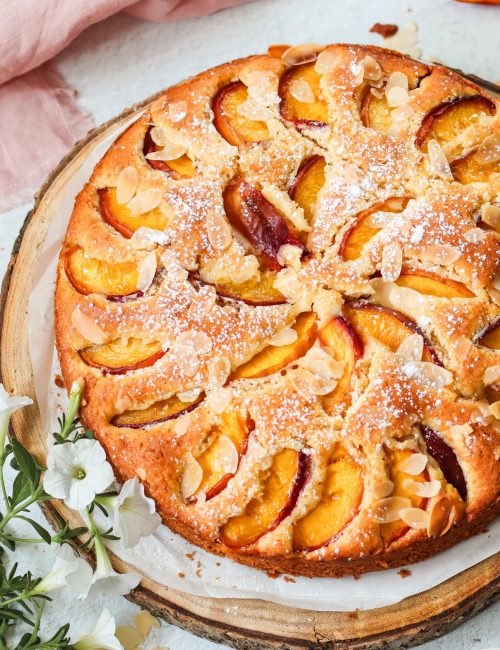 Saftiger Nektarinenkuchen mit Mandeln und Puderzucker auf einer Holzscheibe