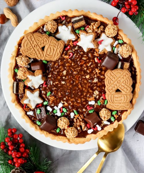 Schokoladen-Walnuss-Tarte mit M&uuml;rbeteigboden, Schokokaramellf&uuml;llung und winterlicher Dekoration aus Keksen, Pralinen und N&uuml;ssen.