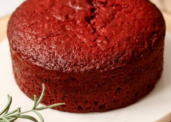 Red Velvet Tortenboden mit saftiger roter Krume auf wei&szlig;em Teller, dekoriert mit Rosmarinzweigen