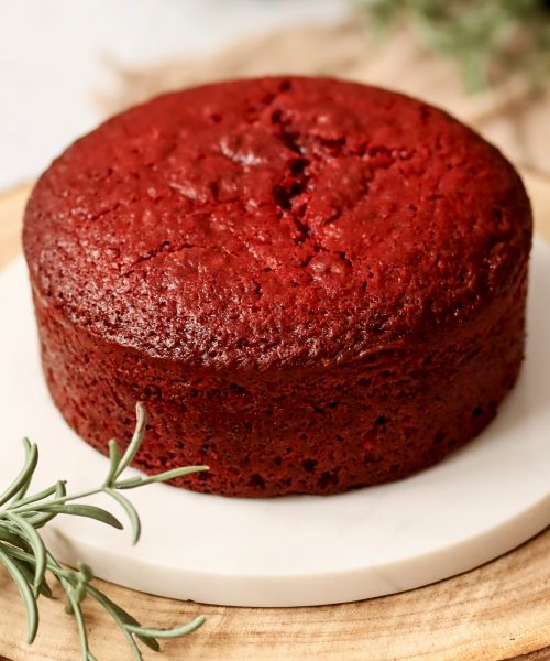 Red Velvet Tortenboden mit saftiger roter Krume auf wei&szlig;em Teller, dekoriert mit Rosmarinzweigen